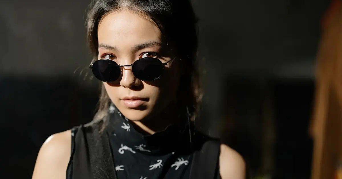 A woman peering over oval sunglasses.